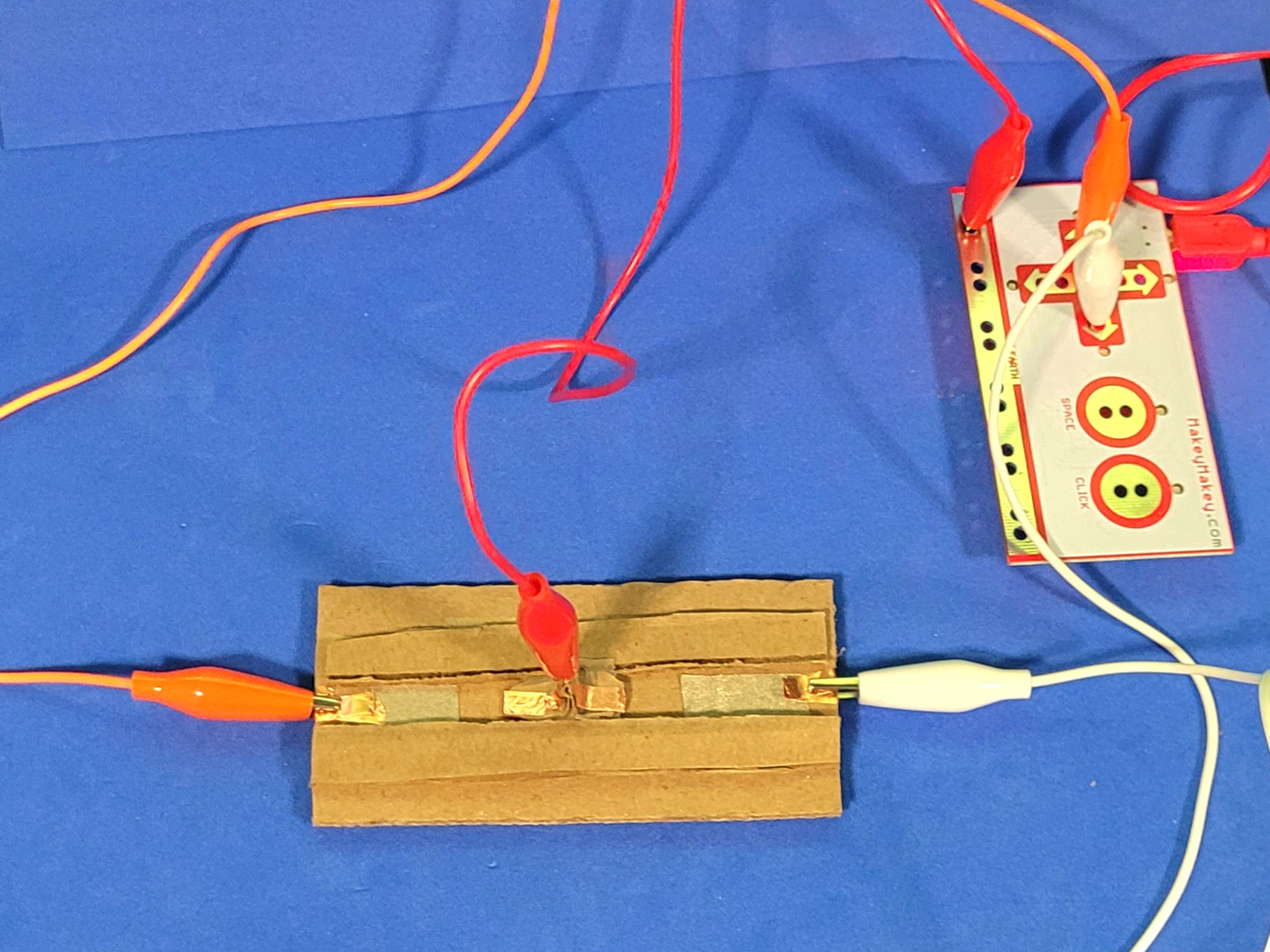A photo of a created cardboard slider. Both sides correspond to different keys that will function as an on and off state for the circuit. The slider part acts as the ground to the MakeyMakey.